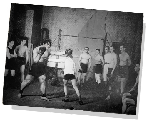 a black and white image of maroh surrounded by a group of men as he boxed another man.